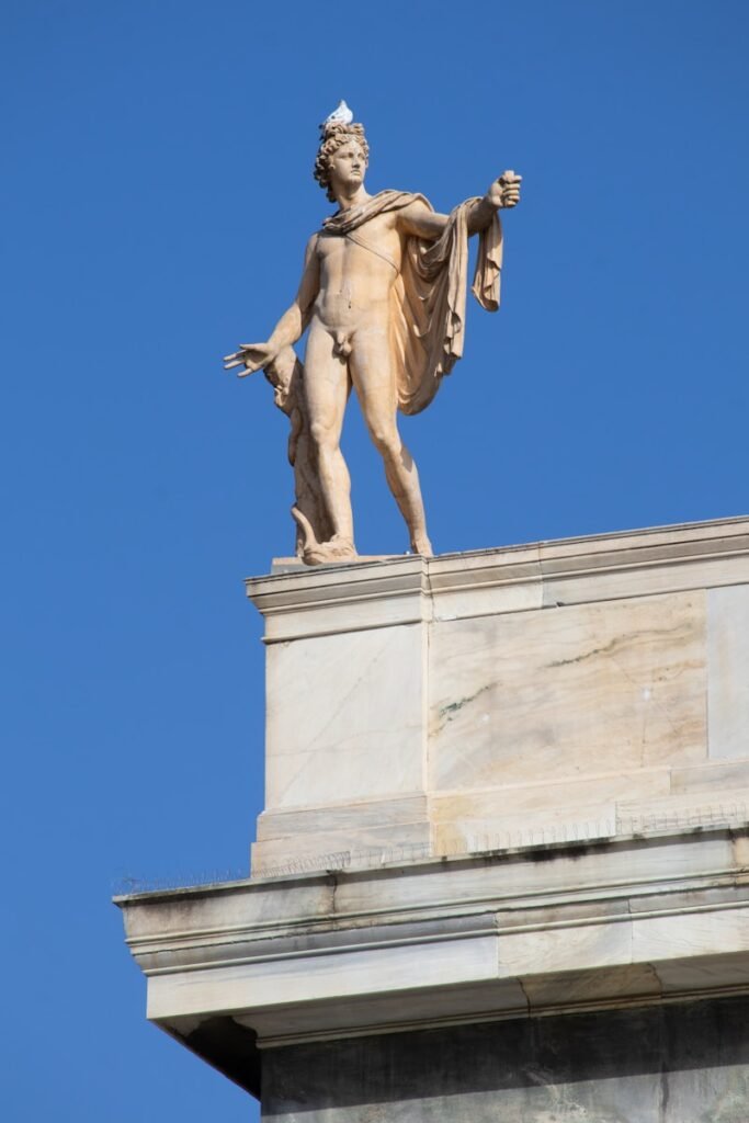 A statue of apollo stands against a blue sky.