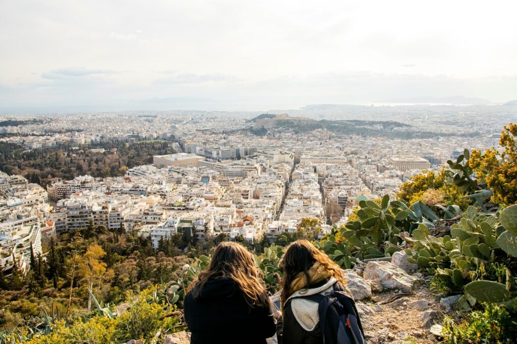 two women sitting on a hill overlooking a city
